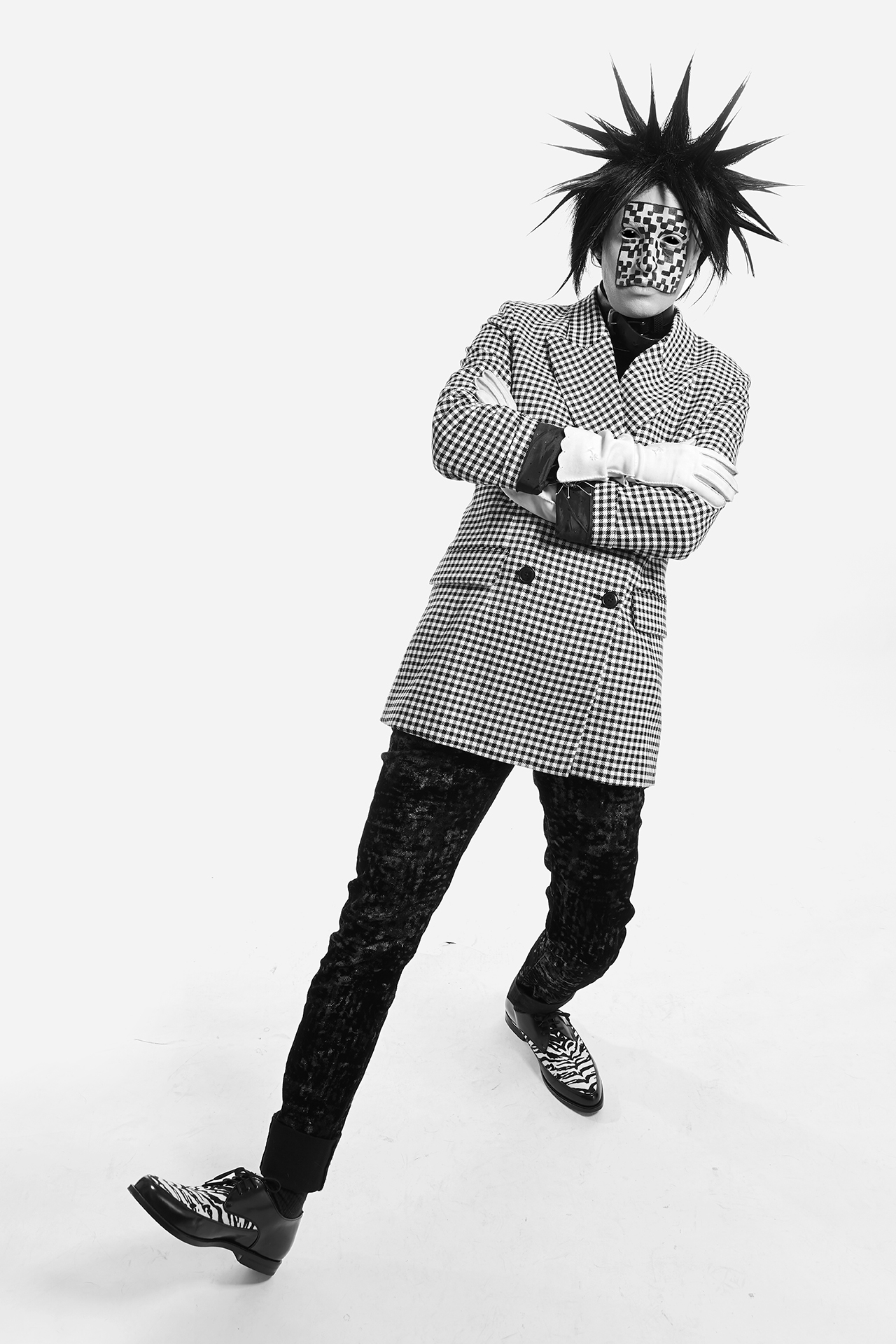 Jesse leaning backwards with checkered facepaint, spiked black hair and a checkered blazer on a white background